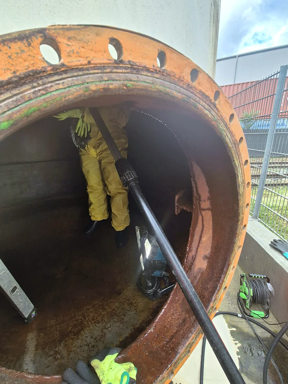 Mitarbeiter in Schutzanzug bei der Reinigung im Inneren eines großen Stahltanks